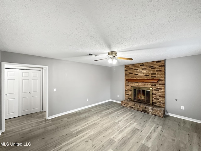 unfurnished living room with ceiling fan, a brick fireplace, a textured ceiling, and dark hardwood / wood-style flooring