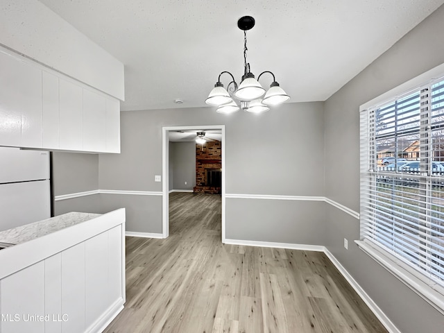 unfurnished dining area featuring a fireplace, ceiling fan with notable chandelier, and light wood-type flooring