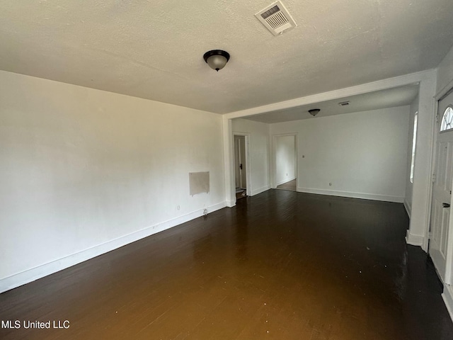 spare room featuring visible vents, a textured ceiling, baseboards, and wood finished floors