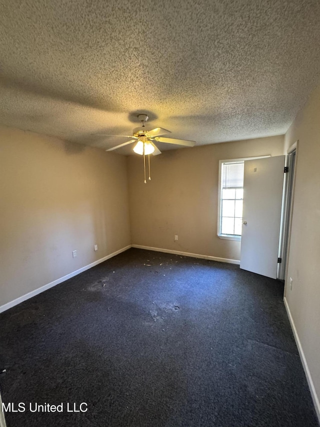 empty room featuring dark colored carpet, ceiling fan, a textured ceiling, and baseboards