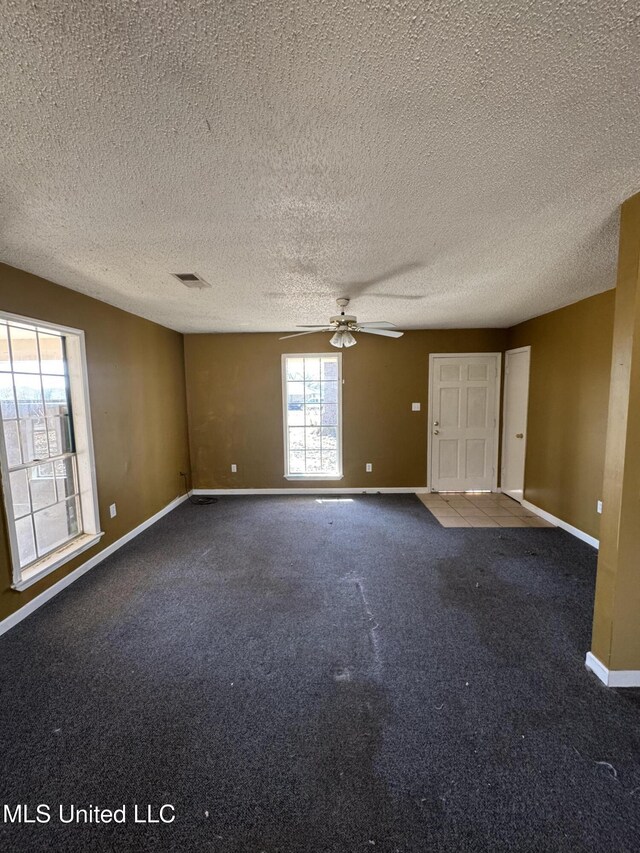 carpeted empty room with visible vents, ceiling fan, a textured ceiling, and baseboards