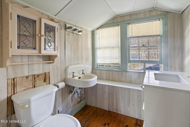 bathroom with wood walls, toilet, vaulted ceiling, wood finished floors, and a sink