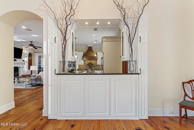 kitchen featuring wall chimney exhaust hood, light hardwood / wood-style flooring, kitchen peninsula, ornamental molding, and white cabinets