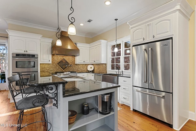 kitchen with light wood-type flooring, hanging light fixtures, stainless steel appliances, white cabinets, and premium range hood