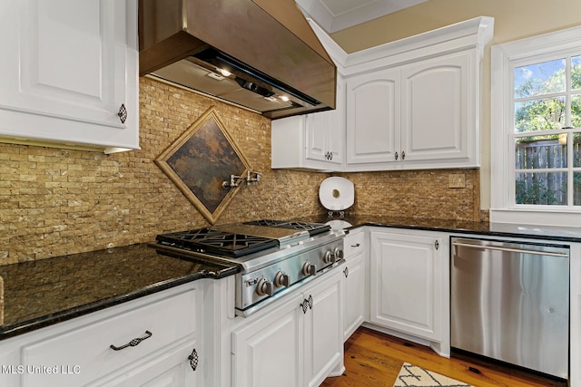 kitchen with tasteful backsplash, wall chimney range hood, appliances with stainless steel finishes, and white cabinets