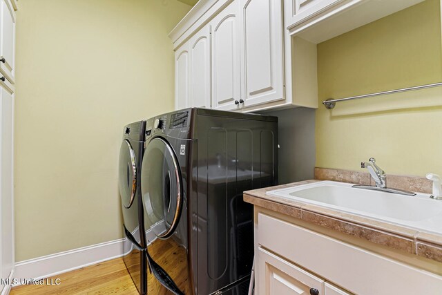 laundry area featuring sink, separate washer and dryer, light hardwood / wood-style floors, and cabinets