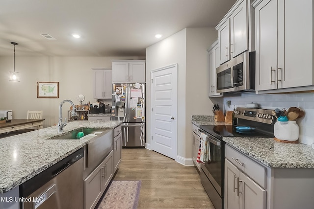 kitchen with sink, light stone counters, light hardwood / wood-style flooring, pendant lighting, and stainless steel appliances