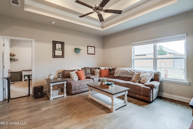 living room featuring wood-type flooring, ornamental molding, a raised ceiling, and ceiling fan