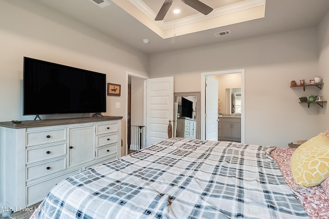 bedroom with crown molding, connected bathroom, and a tray ceiling