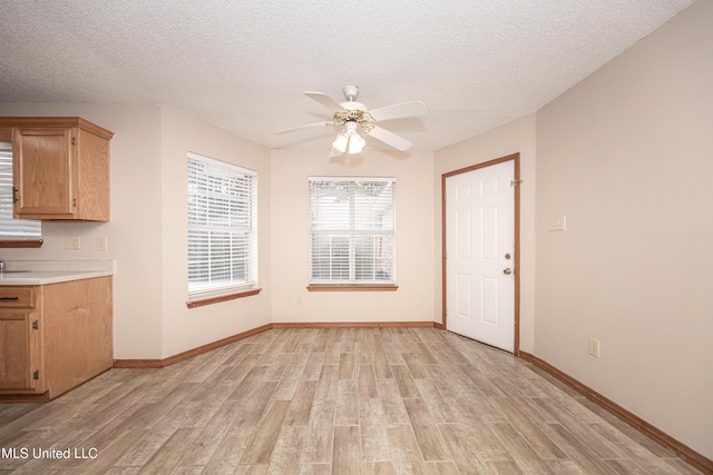 unfurnished dining area with ceiling fan, a textured ceiling, and light wood-type flooring