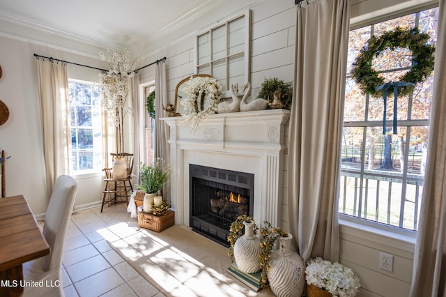 sitting room with a healthy amount of sunlight, light tile patterned floors, crown molding, and a tiled fireplace