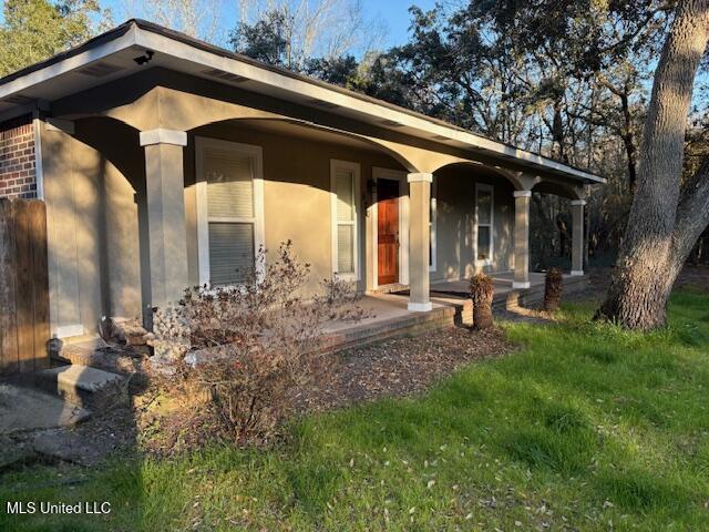 doorway to property with covered porch, a lawn, and stucco siding