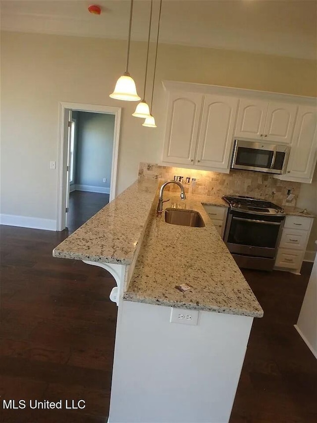 kitchen with light stone countertops, a peninsula, a sink, white cabinets, and appliances with stainless steel finishes