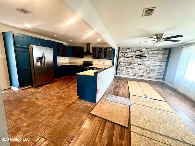 kitchen featuring appliances with stainless steel finishes, dark hardwood / wood-style floors, blue cabinets, sink, and wall chimney range hood