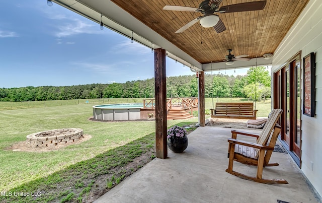 view of patio featuring a fenced in pool, a fenced backyard, a forest view, a ceiling fan, and a fire pit