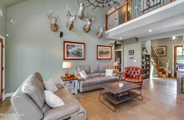 living room featuring finished concrete flooring, stairway, baseboards, a high ceiling, and recessed lighting