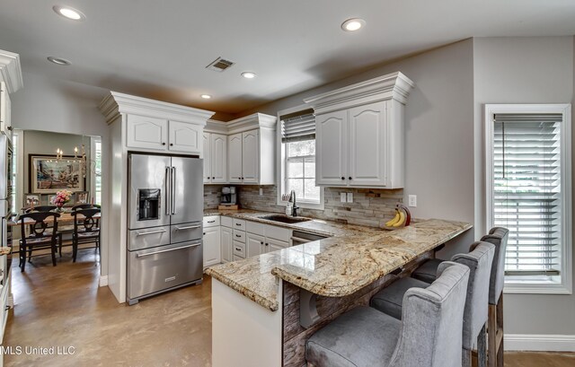 kitchen with appliances with stainless steel finishes, a sink, a peninsula, backsplash, and visible vents