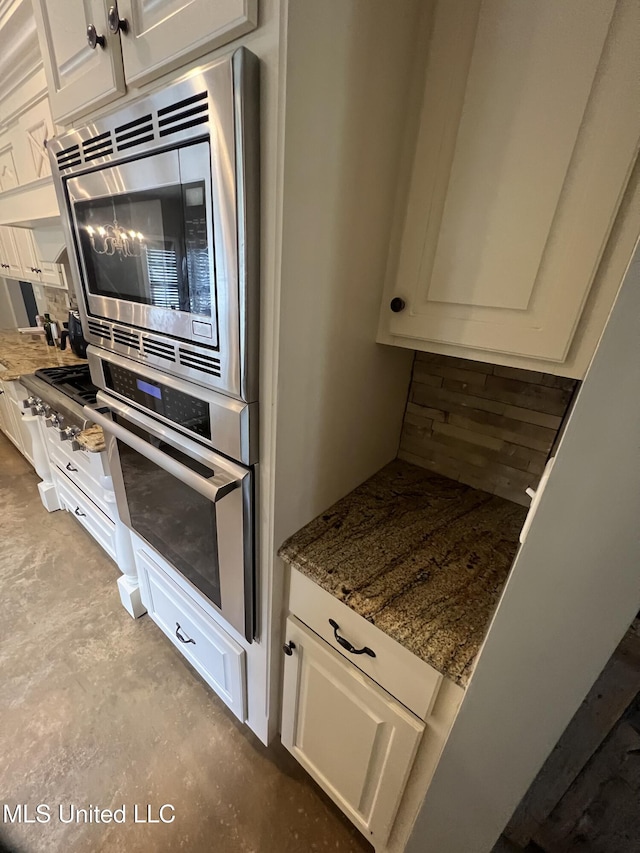 kitchen featuring dark stone counters, appliances with stainless steel finishes, white cabinets, and concrete flooring