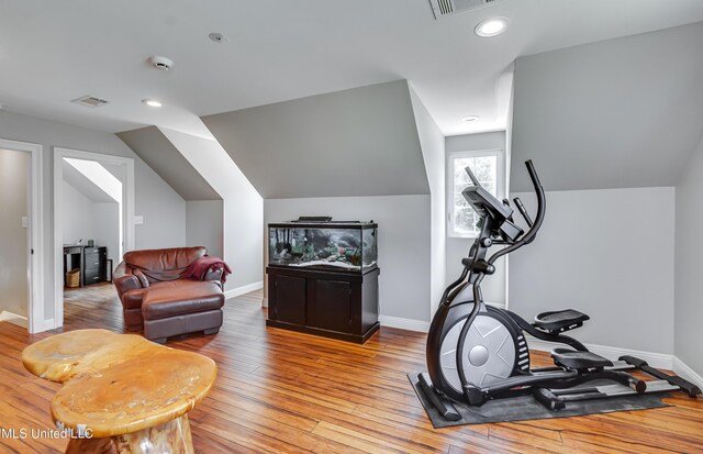 exercise room with baseboards, lofted ceiling, light wood-type flooring, and visible vents