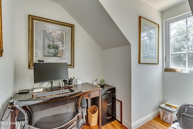 office area with baseboards, light wood-style flooring, a healthy amount of sunlight, and vaulted ceiling