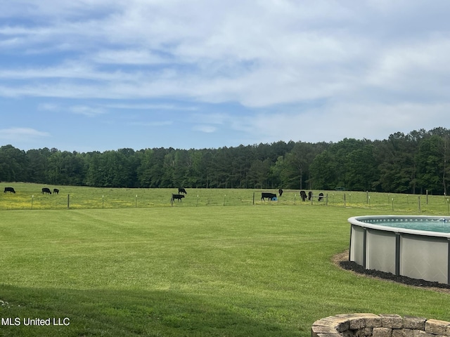 view of yard with a fenced in pool, a view of trees, fence, and a rural view