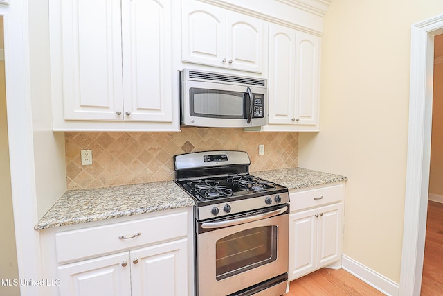 kitchen with light stone countertops, light wood finished floors, stainless steel appliances, baseboards, and backsplash