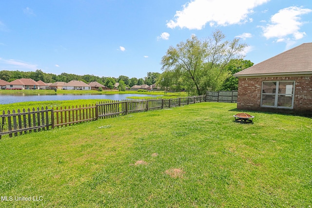 view of yard featuring a water view, a fire pit, and a fenced backyard