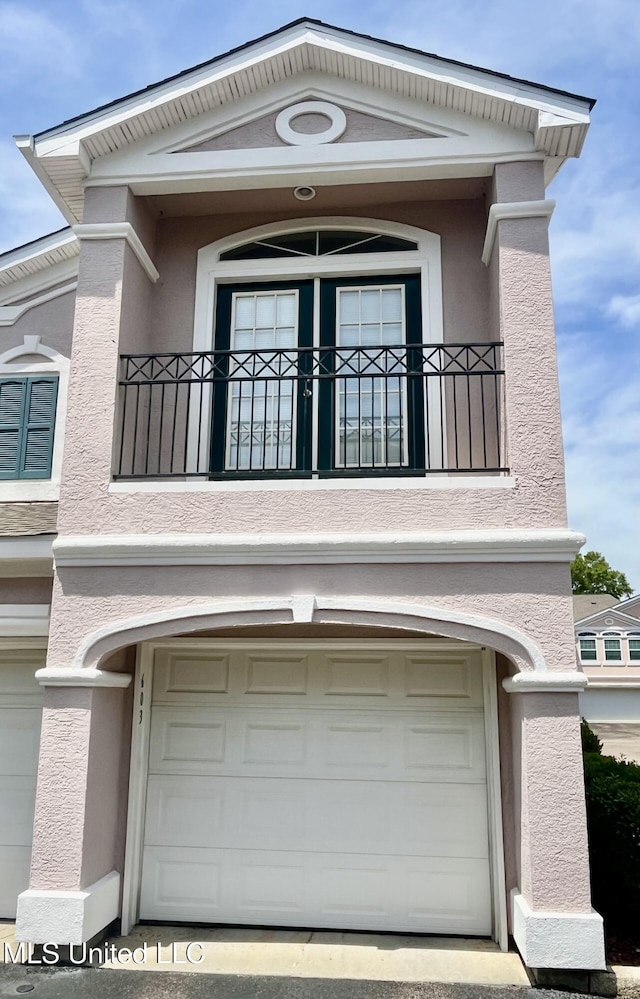 view of side of property with an attached garage, a balcony, and stucco siding