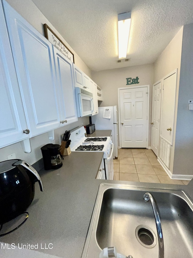 kitchen featuring a textured ceiling, visible vents, light tile patterned floors, white cabinets, and white appliances