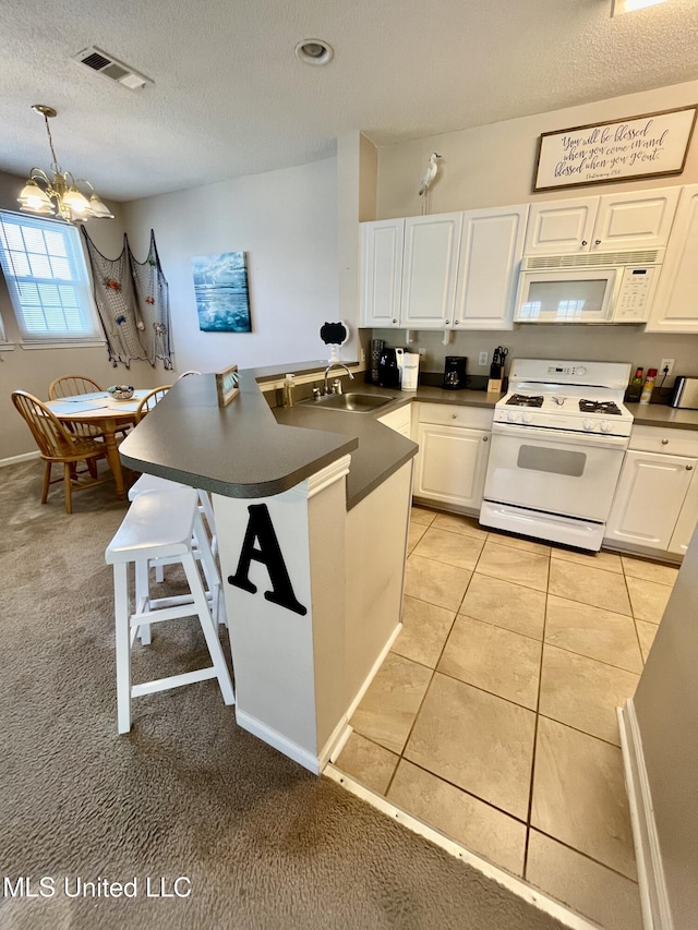 kitchen with visible vents, dark countertops, a sink, a peninsula, and white appliances