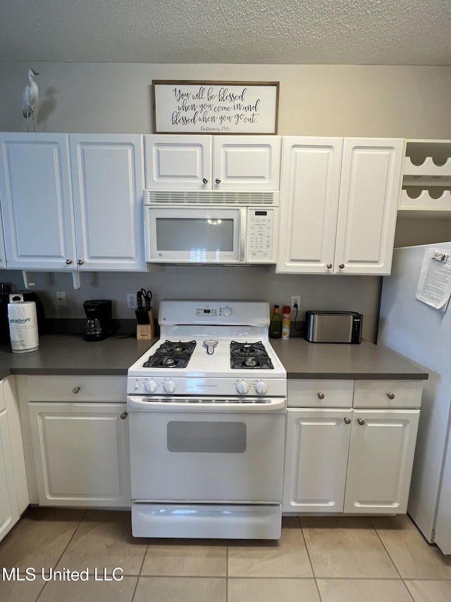 kitchen featuring a textured ceiling, light tile patterned floors, white cabinets, and white appliances