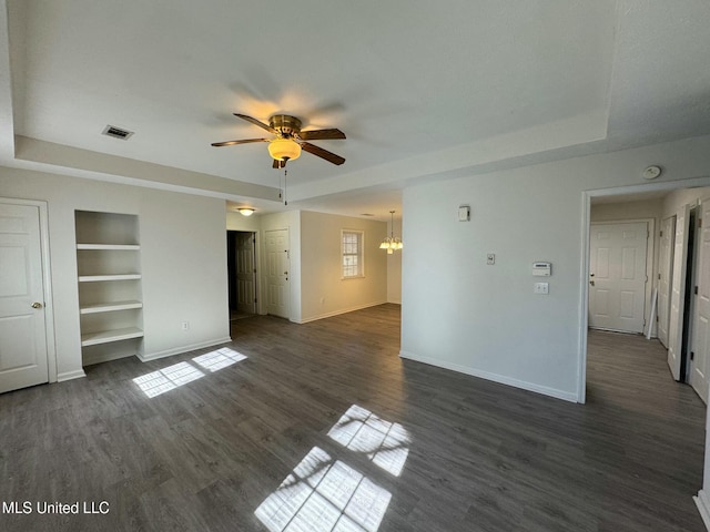 unfurnished living room featuring ceiling fan with notable chandelier, built in features, dark wood-type flooring, and a tray ceiling