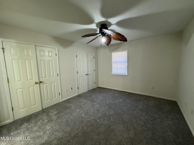 unfurnished bedroom with ceiling fan, dark carpet, and two closets