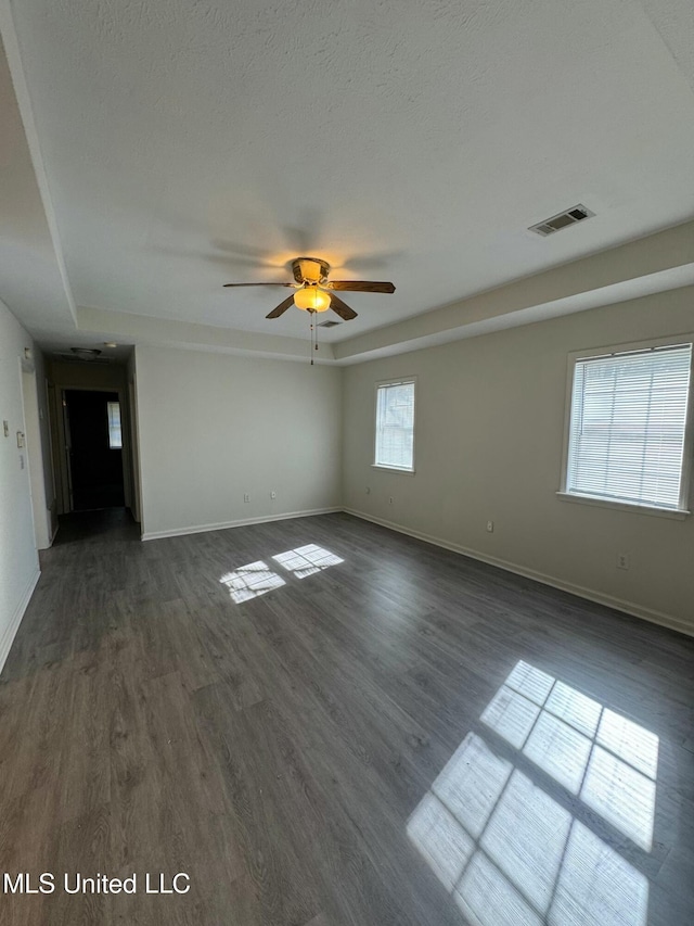 empty room featuring a raised ceiling, ceiling fan, dark hardwood / wood-style flooring, and a textured ceiling