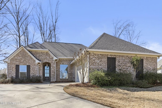 french provincial home featuring brick siding, driveway, an attached garage, and roof with shingles