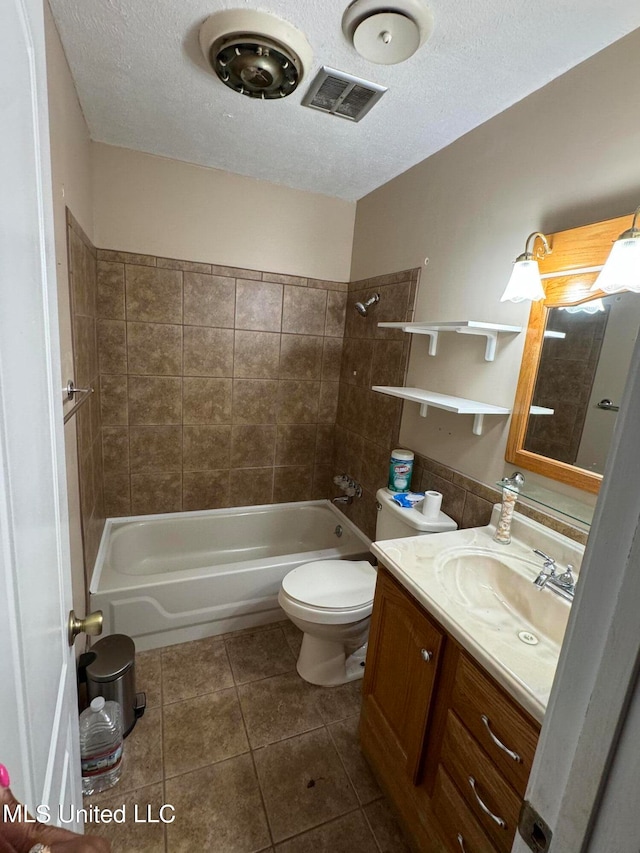 full bathroom featuring a textured ceiling, toilet, vanity, tiled shower / bath combo, and tile patterned floors