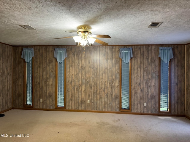 carpeted spare room featuring wooden walls, a textured ceiling, and ceiling fan