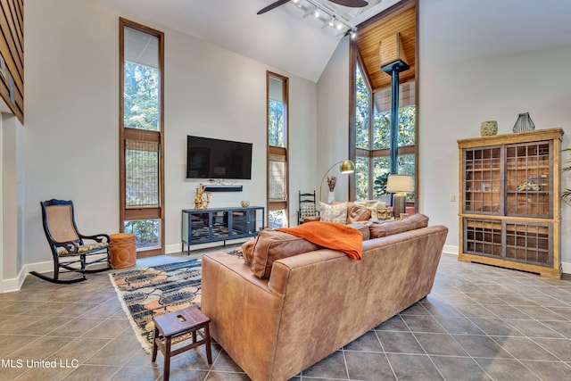 living room with a wood stove, rail lighting, ceiling fan, high vaulted ceiling, and tile patterned flooring