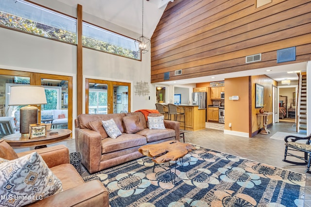 living room with a chandelier, high vaulted ceiling, light tile patterned flooring, french doors, and wooden walls