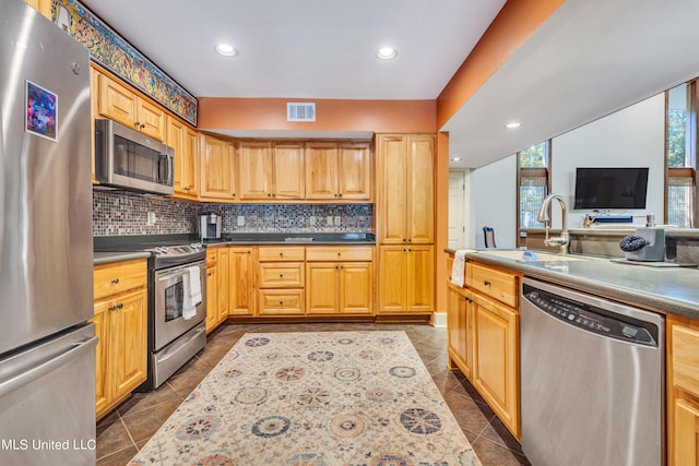 kitchen with dark tile patterned flooring, light brown cabinetry, sink, backsplash, and stainless steel appliances