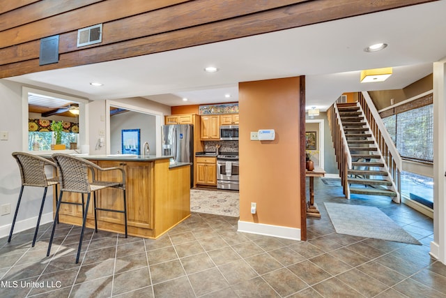 kitchen featuring kitchen peninsula, ceiling fan, backsplash, a kitchen bar, and stainless steel appliances