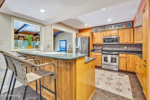 kitchen with dark tile patterned floors, decorative backsplash, sink, a kitchen bar, and appliances with stainless steel finishes