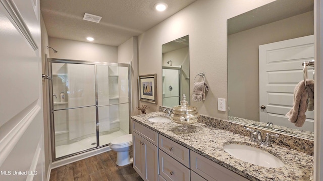 bathroom with hardwood / wood-style flooring, toilet, a shower with shower door, vanity, and a textured ceiling