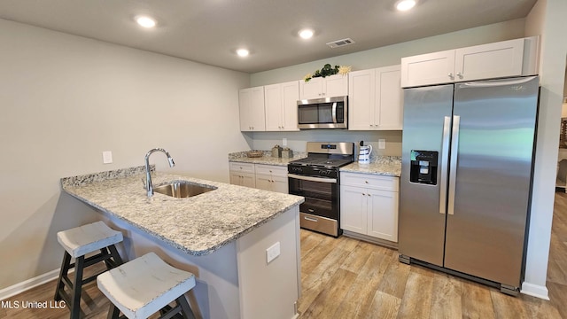 kitchen featuring kitchen peninsula, stainless steel appliances, sink, a breakfast bar, and white cabinets