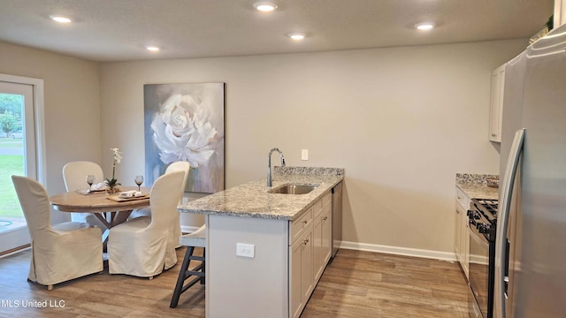 kitchen with sink, light stone countertops, white cabinets, light wood-type flooring, and appliances with stainless steel finishes