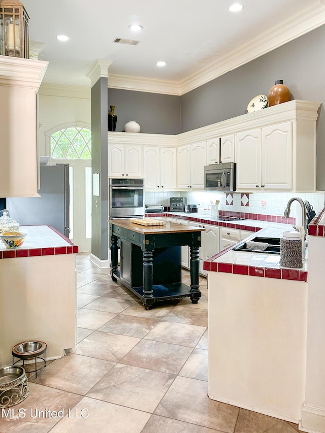 1120 Ford Rd, Terry, MS 39170 - kitchen featuring appliances with stainless steel finishes, tile countertops, tasteful backsplash, ornamental molding, and white cabinetry