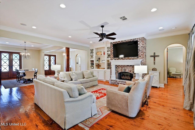 living area featuring ornamental molding, light wood-style flooring, visible vents, arched walkways, and built in shelves