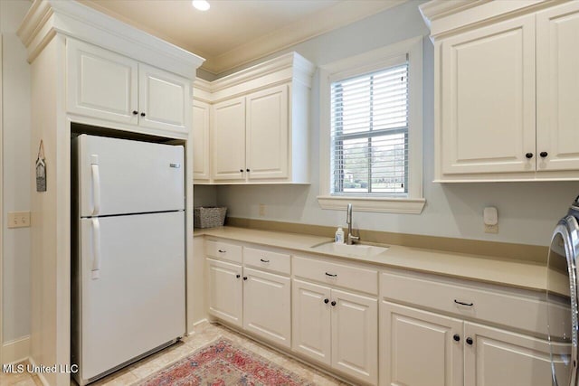 kitchen featuring light countertops, a sink, freestanding refrigerator, and white cabinetry