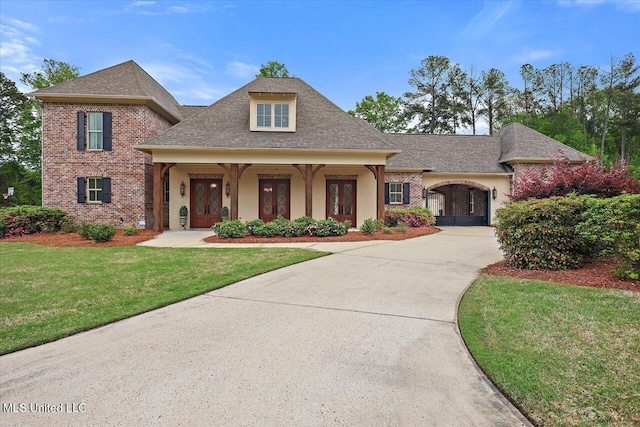 view of front of property with roof with shingles, stucco siding, driveway, a front lawn, and brick siding