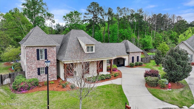 view of front of home featuring fence, brick siding, a front lawn, driveway, and roof with shingles